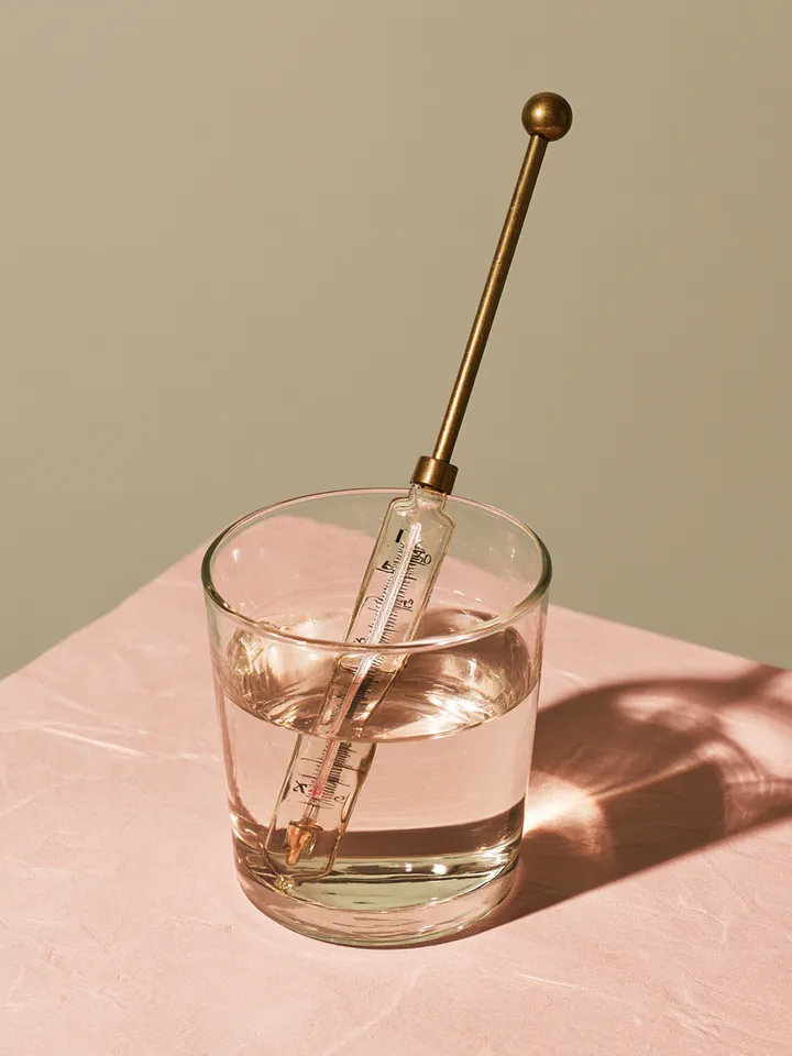 Vintage brass thermometer standing in a glass of water, symbolizing how a Happy Money loan rate reflects credit risk
