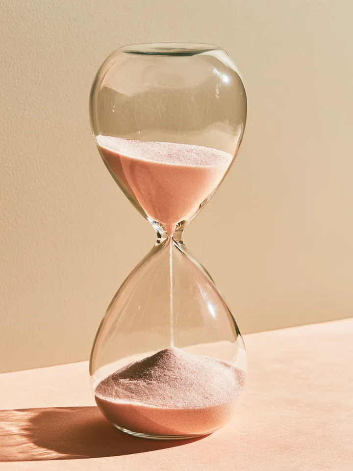 Hourglass with pale pink sand half run through, symbolizing the short term of a Happy Money loan